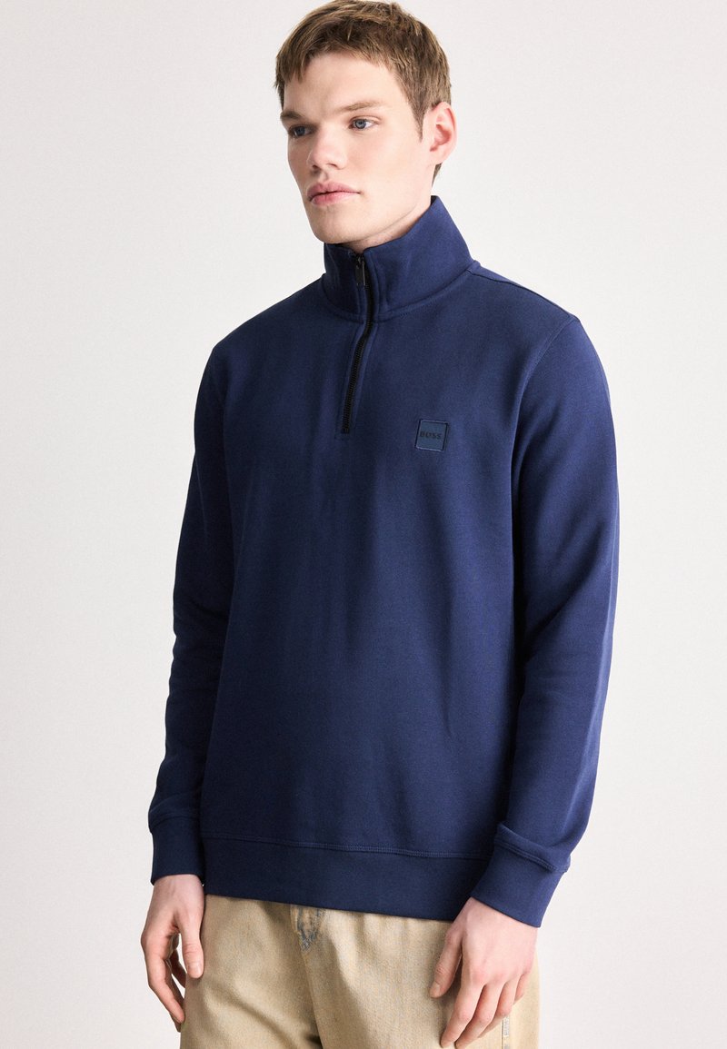 Ναυτικό μπλουζάκι με κουκούλα από μαλακό ύφασμα, με γιακά με φερμουάρ μέχρι τη μέση, ριμπ μανσέτες και μικρό μαύρο λογότυπο στο στήθος.