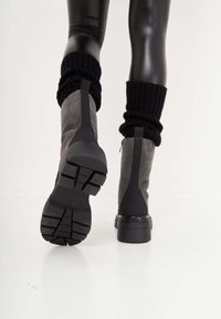 Gray suede ankle boots with black rubber accents, featuring a thick tread sole and ribbed knit leg warmers. Smooth texture, modern design.