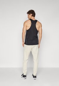 Black tank top with a racerback design, paired with beige joggers. Features minimal stitching details and black athletic shoes.