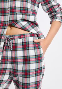 Ensemble de pyjama en flanelle à carreaux rouges, verts et blancs comprenant une chemise à boutons et un pantalon à taille élastique avec poches et cordon de serrage.