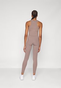 Bruine aansluitende tanktop en leggings, gemaakt van rekbaar materiaal. Gladde textuur met een racerback-ontwerp en minimale branding.