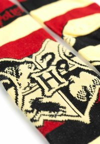 Calzini lavorati a maglia caratterizzati da strisce rosse e nere, base colore crema e un design con uno stemma nero con una grande "H" al centro.