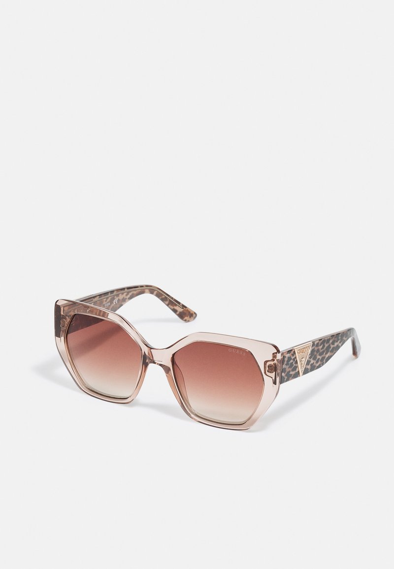 Ochelari de soare supradimensionați de formă hexagonală cu un cadru transparent piersiciu, lentile cu gradient maro și brațe cu imprimeu leopard, având un accent metalic cu logo.