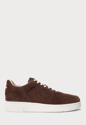 Brązowy zamszowy sneaker z białymi sznurówkami i grubą białą podeszwą, z małym haftowanym logo po boku.