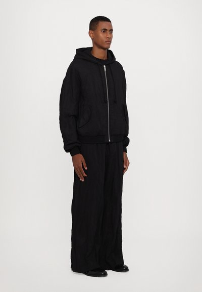 Svart zip-up hoodie med dragsko på huva och två framfickor, kombinerad med vida svarta byxor, båda i strukturerad tyg.