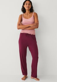 Light pink tank top with lace trim, paired with dark burgundy, loose-fitting drawstring pajama pants. Comfortable, soft fabric with relaxed fit.