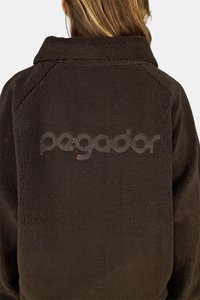 Pruun villane jope volditud kraega, millel on tekstuuriga sisemus ja suur reliefne logo seljal.