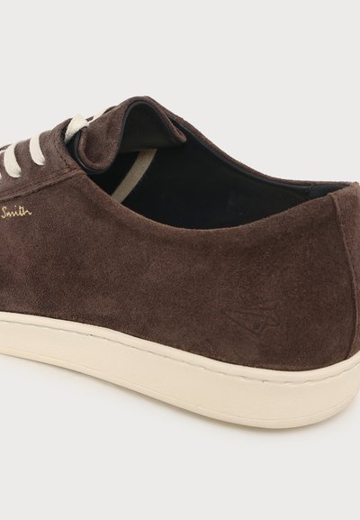 Baskets en daim marron avec lacets blancs et semelle beige, montrant les détails latéraux et arrière sur un fond clair uni.