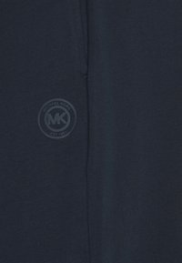 Marineblå bomull T-skjorte med et rundt logo som har "Michael Kors" og "MK" trykt i en kontrasterende farge. Jevn tekstur, kortermet.