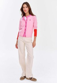 Różowo-czerwony kardigan w blokowane kolory z małym emblematem serca, wykonany z miękkiego materiału dzianinowego, z guzikami i prążkowanymi mankietami.