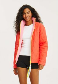 Prošívaná bunda s živým korálovým vnějškem, světlými růžovými podšívkami a žlutým zipem. Obsahuje stahovací šňůrku a design s barevnými bloky.