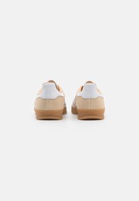 Beige och vita sneakers med en slät läderutsida, gummisulor och en minimalistisk design. Har en mjuk, texturerad baksida och sidodetaljer.