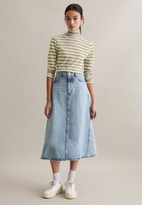 Zielony oliwkowy top w paski z długim rękawem i wysokim kołnierzem, zestawiony ze spódnicą midi z jasnoniebieskiego denimu, noszony z białymi trampkami i krótkimi skarpetkami.