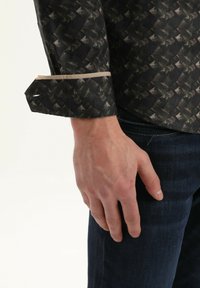 Camisa de manga larga negra con un diseño geométrico, con un borde de puño de color claro. Llevada con jeans de mezclilla oscura.