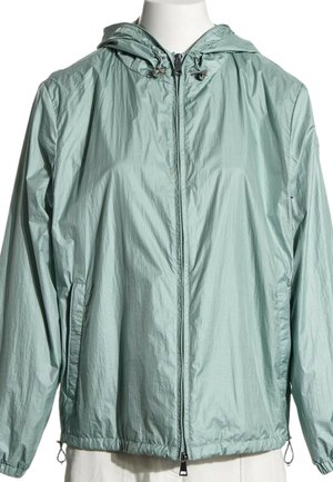 Chaqueta cortavientos con capucha de color verde claro, cremallera frontal, capucha con cordón, puños elásticos y bolsillos laterales en un torso de maniquí blanco.