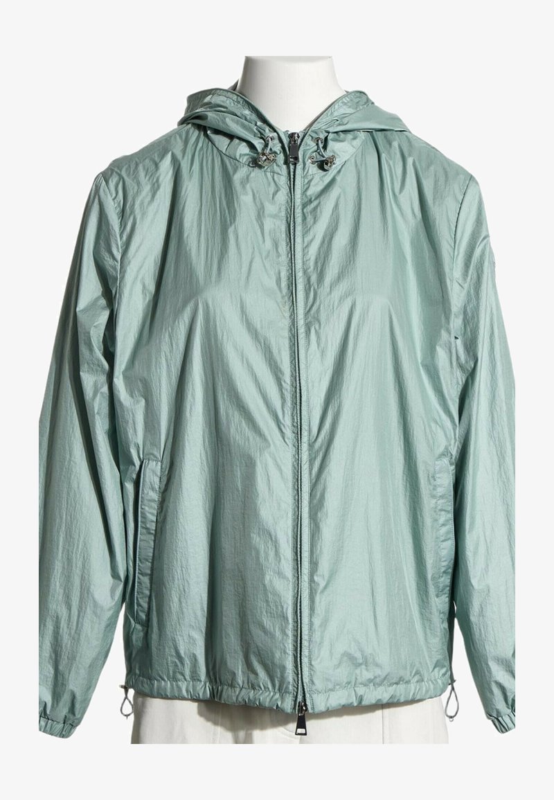 Veste coupe-vent à capuche vert clair avec fermeture éclair sur le devant, capuche à cordon, poignets élastiques et poches latérales sur un torse de mannequin blanc.