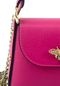 Fuchsia leren handtas met een flap sluiting, gouden vlinderaccent en een gouden kettinghangertje. Textuur oppervlak en zichtbare stikdetails.