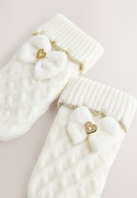 Fehér kötött zokni texturált gyémántmintával, bordázott szegéllyel, puha masni díszítéssel és arany szív alakú díszítéssel minden zoknin.