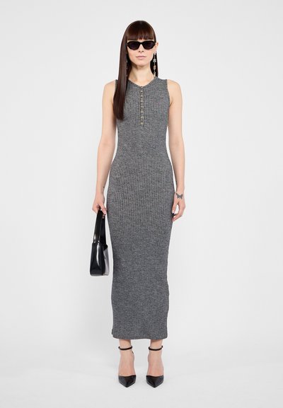 Hallide ribaga dress maksikleid, millel on kõrge kaelus, nööbid ja kehaäratav siluett. Kandnud mustade päikeseprillide ja käekotiga.