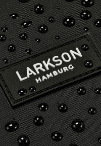 Svart texturerad tyg med vattendroppar och en rektangulär etikett som säger "LARKSON HAMBURG" i vita bokstäver.