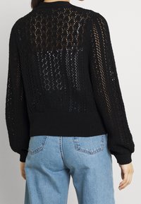 Maglione nero a maglia con un motivo in pizzo, maniche lunghe e orlo a coste. Indossato sopra jeans azzurri chiari, mette in evidenza una vestibilità morbida.