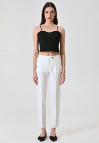 Zwarte crop top met dunne bandjes, gecombineerd met op maat gemaakte witte broek met een knoopdetail, aangevuld met zwarte ballerina's met strik.