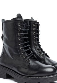 Botas de cuero negro con cordones, acabado suave, puntera redonda y suela gruesa con relieve. Cuenta con ojales de metal y una cinta en la parte de atrás para facilitar el calzado.