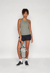 Treningsantrekk med en tettsittende, olivengrønn singlet og svarte shorts. Tilbehør inkluderer en tenniskølle og svarte joggesko.