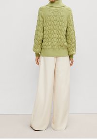 Strukturierter grüner Strickpullover mit hoch geschlossenem Kragen und Ballonärmeln, kombiniert mit cremefarbenen, weit geschnittenen Hosen.