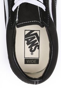 Czarny płócienny but na białych sznurowadłach, o szerokim kroju. Wnętrze pokazuje jasną wkładkę z logo "VANS" i napisem "WIDE".