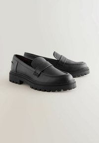 Musta nahkainen loaferit, joissa on teksturoitu pinta, etuhihnalla ja paksulla kumipohjalla, jossa on urat pitoon.