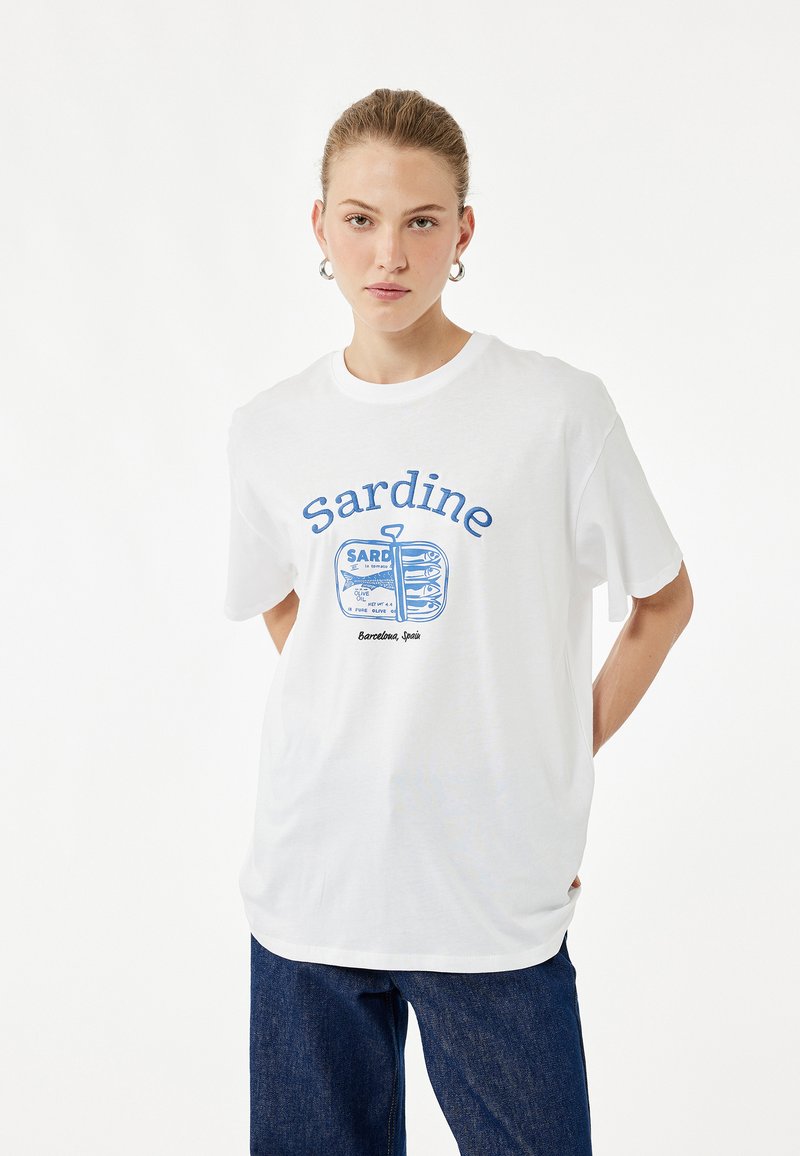 Witte katoenen t-shirt met blauwe grafische tekst "Sardine" en een illustratie van een sardineblik. Korte mouwen, ronde hals, relaxte fit.