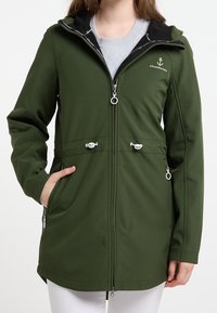 Veste softshell verte avec fermeture éclair sur le devant, capuche et poches latérales. Éléments métalliques argentés et logo sur le côté supérieur gauche.
