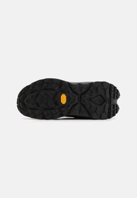 Musta kumisaappaan pohja, jossa on teksturoitu pitoesine ja keltainen Vibram-logo. Suunnittelussa on syviä uria ja karhea reuna.