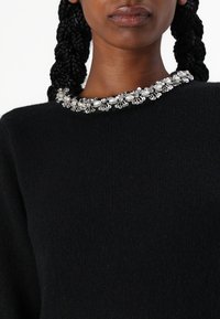 Pull noir avec un col orné de détails argentés et de perles. La texture semble douce et tricotée.