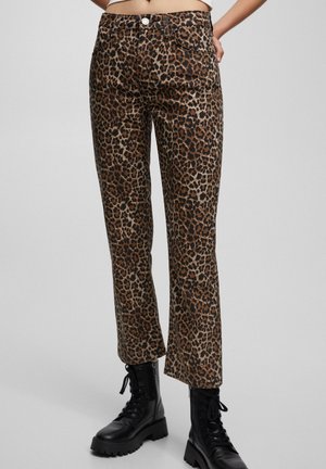 Leopardmønstrede bukser med lige ben kombineret med sorte snørebånds combatstøvler, båret af en person med hænderne på hofterne.