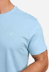 Lyseblå bomulls t-skjorte med rund hals og korte ermer. En liten hvit logo med "EST 1993" er trykket på venstre bryst.
