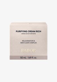 Kvadratisk, gräddfärgad låda märkt "Purifying Cream Rich." Texten är svart och guld, och innehåller detaljer som "50 mL" och "Babor." Slät textur.