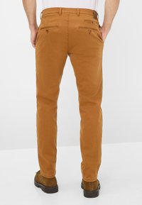 Braune Baumwollhosen mit geradem Bein, ausgestattet mit zwei Gesäßtaschen mit Knopfverschluss und dezenten Nähten.