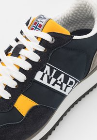 Sneaker blu navy con accenti gialli. Presenta lacci bianchi, materiale scamosciato testurizzato e sintetico, e una striscia con il marchio sul lato.