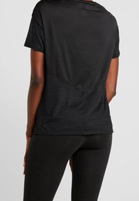 Black athletic t-shirt featuring a textured mesh back, short sleeves, and a rounded hem, paired with black leggings for a functional look.