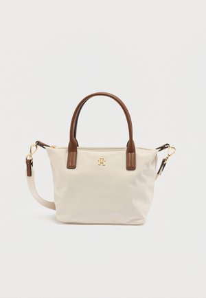Petit sac à main beige avec poignées marron, logo doré sur le devant, et bandoulière beige réglable avec fermoirs dorés sur fond blanc.