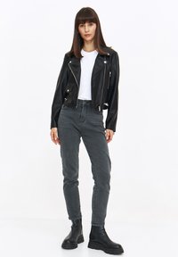 Czarna skórzana kurtka motocyklowa z srebrnymi zamkami, biała koszulka, szare dżinsy oraz czarne botki za kostkę z grubą podeszwą.