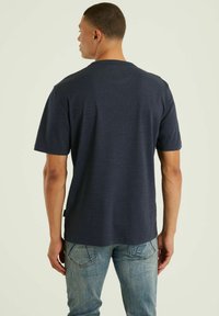 T-paita tummansinistä väriä lyhyillä hihoilla ja pyöreällä kaula-aukolla, pehmeästä puuvillasekoitteesta valmistettu, suora helma, yhdistettynä vaaleansiinisiin farkkuihin.