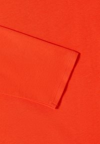 Tissu orange vif uni avec un ourlet cousu visible et un détail de bord plié.