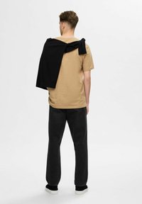 Beige t-shirt with a round neck, paired with black pants and black shoes. A black sweater is draped over the shoulders.
