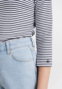 Randig långärmad topp i marinblå och vit bomull, med en liten broderad detalj på ärmen; kombinerad med ljusblå denimjeans.