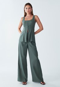 Groen tweedelig ensemble met een nauwsluitend bovenstuk met een vierkante halslijn en een knoopsluiting aan de voorkant, gecombineerd met wijde, vloeiende broekspijpen.