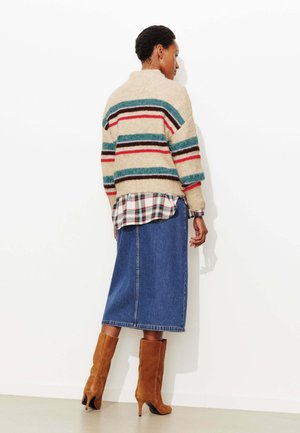 Pull beige à rayures bleu sarcelle, superposé sur une chemise à carreaux, associé à une jupe en jean et des bottes à talons en daim marron.