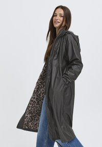 Sort letvægts regnfrakke med hætte, der har en leopardprint-foring og lommer. Stofdet har en glat, blank overflade.